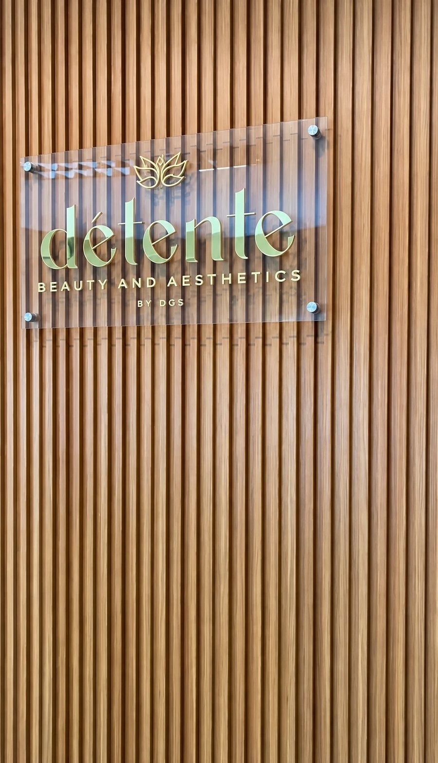 D&eacute;tente Beauty and Aesthetics by DGS sign on a wood-slat wall at the studio